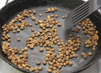Green coffee beans roasting on the black pan