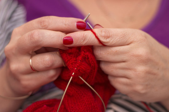 Woman knits with knitting needles red sweater from natural woolen threads