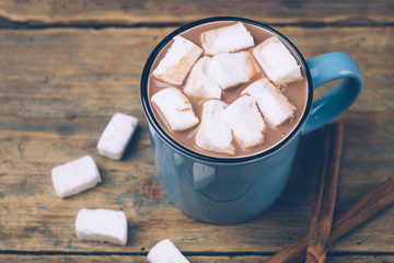 Cup of hot cocoa or hot chocolate with marshmallows and cinnamon sticks on wooden background. Winter mood.