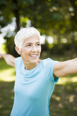 Senior woman exercising tretching arm in the park