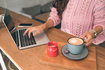 partial view of female freelancer working on laptop while sitting at table with smartphone and coffee cup in cafe