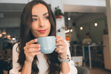 selective focus of young attractive woman drinking coffee at table in cafe