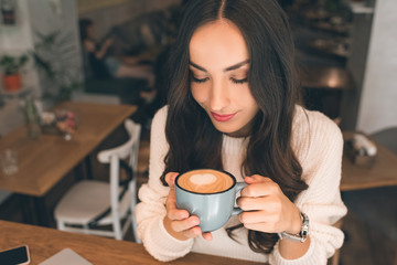 high angle view of young attractive woman drinking coffee at table in cafe