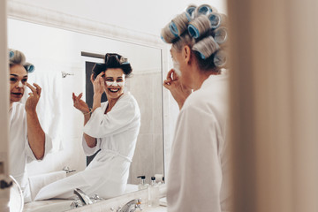 Happy mother and daughter applying face cream standing in the ba