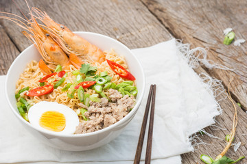 Closed up instant noodles with vegetables, egg,shrimps, minced pork  in bowl on wood background, junk food or fast food concept.selective focus
