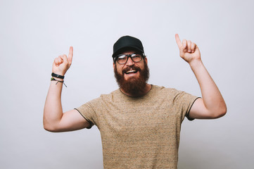 Young bearded man pointing up with both hands smiling at the camera.