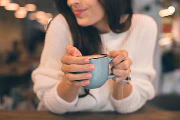 partial view of woman holding coffee cup at table in cafe