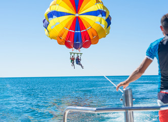 Happy couple Parasailing in Dominicana beach in summer. Couple under parachute hanging mid air. Having fun. Tropical Paradise. Positive human emotions, feelings, family, children, travel, vacation. 