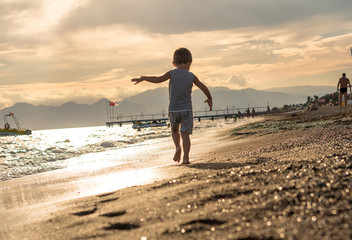 Smiling little boy playing in the sea on the sunset. Positive human emotions, feelings, joy. Portrait of happy little kid boy on the beach of ocean. Funny cute child making vacations, enjoying summer.