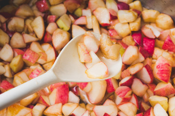 apple jam making in process, focus on the apple pieces cupping up in the white ladle with boiling juice in the background