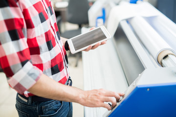 Faceless side view of casual worker holding tablet and setting machine for printing working in publishing house