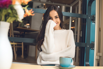 smiling pretty woman sitting at table with coffee cup in cafe