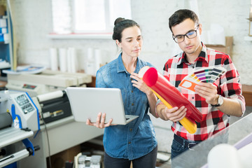 Young man and woman with palette of colors and laptop working in team on new design project