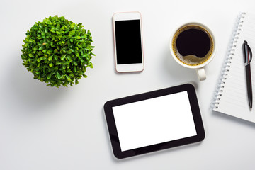 Mock up of office desk with blank white screen tablet pc, blank black screen smartphone, coffee cup, notebook, pen and plant pot, top view design