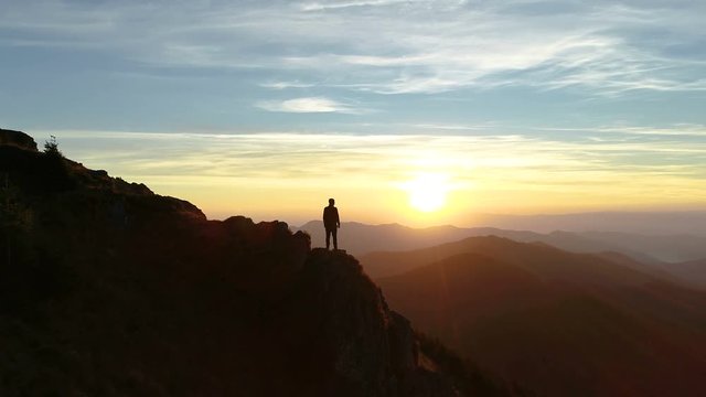 The male standing on the mountain and enjoying the picturesque sunset
