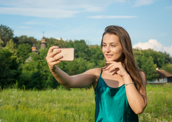 Young beautiful woman doing selfie on a smartphone at the rural background in summer.