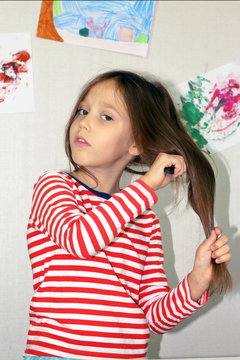 child girl combs her long hair, is in the nursery with pictures on the wall