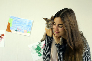 young attractive brunette woman playing with a Sphinx kitten hugging an animal