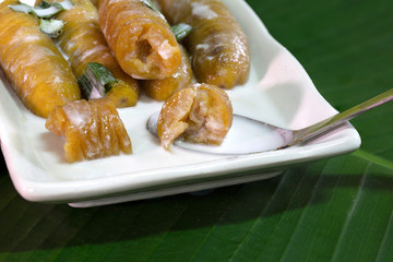 Banana in syrup with coconut milk and pandan leaf for smell in long white dish on green banana leaf