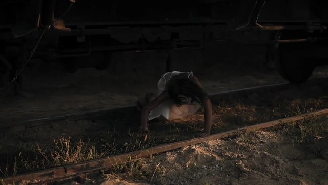 A wounded female zombie in bloody white dress climbs out from under the wagon on the railway and walks away. Halloween, filming, staging concept