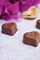 Chocolate hearts sprinkled with pink glitter, pink bougainvillea flowers and a candle