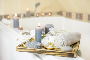 Candles burning and spa essentials on wooden tray in bathroom, essential oil, bath salt on wooden...