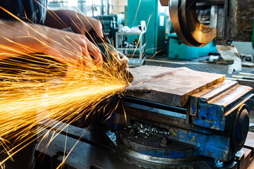 The worker polishes the metal with a grinding machine and sparks close-up.