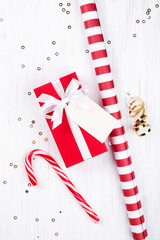 Christmas gift wrapped in red paper tied with white ribbon on white wooden background decorated with sparkles. Flat lay, copy space.