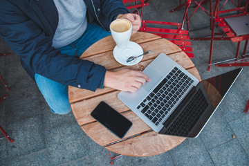 young adult man working on laptop at outdoors cafe with cup of latte