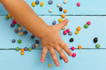 The child pulls his hand to the colored candy on the blue table