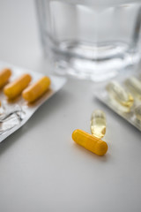 Zwei Pillenblister mit gelben Kapseln und Tabletten und Wasser Glas