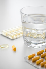 Zwei Pillenblister mit gelben Kapseln und Tabletten und Wasser Glas