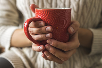 Women's hands in sweater are holding cup of hot coffee, chocolate or tea. Concept winter comfort,...