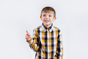 A little boy in a plaid shirt on a white background raised his finger up and something came up