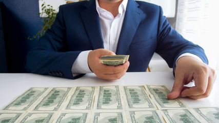 Closeup photo of successful businessman laying money in front of him on office desk