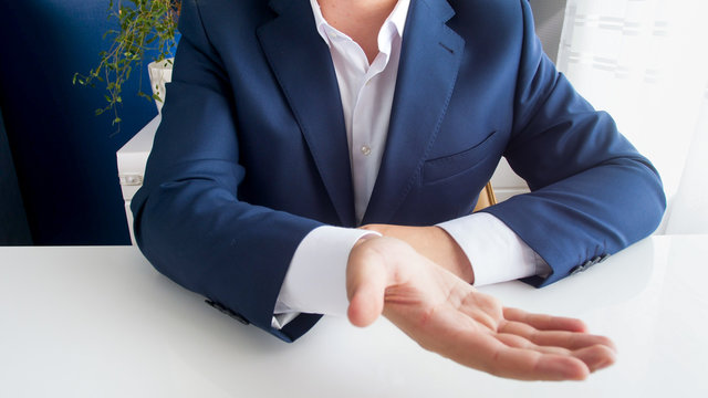 Closeup image of businessman sitting behind office desk stretching hand and asking for money