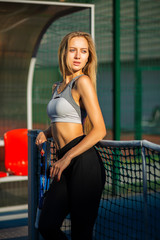 Glamorous blonde model with perfect body posing with a tennis racket at the court