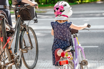 Mother with her kids in helmets riding bicycle at city street, family transportation concept