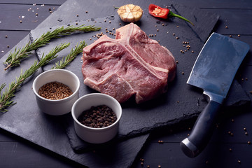 a big raw t-bone steak with spices lying on a dark wooden table, top view