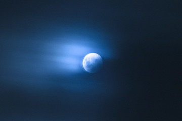 Naklejka na ściany i meble Clouds moving over bright blue full moon