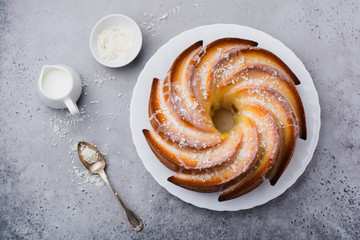 Bundt cake with sugar glaze and coconut on dark grey old concrete background. Selective focus. Top...
