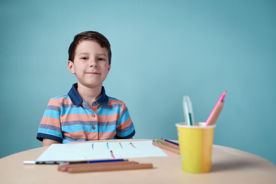 Cheerful smiling Caucasian boy spending time drawing with colorful pencils at home. He is looking into the camera.
