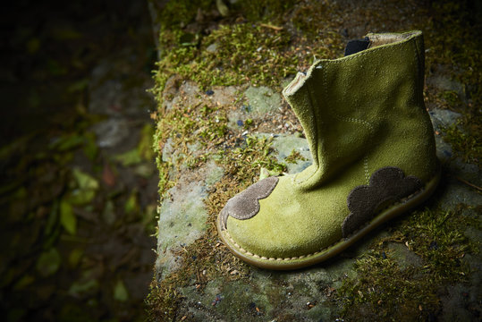 Abandoned baby shoe lying on an old stone covered with moss. Lost children's shoes.