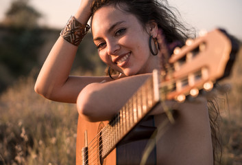 Smiling Naked Curly brunette girl Sitting with guitar in the field