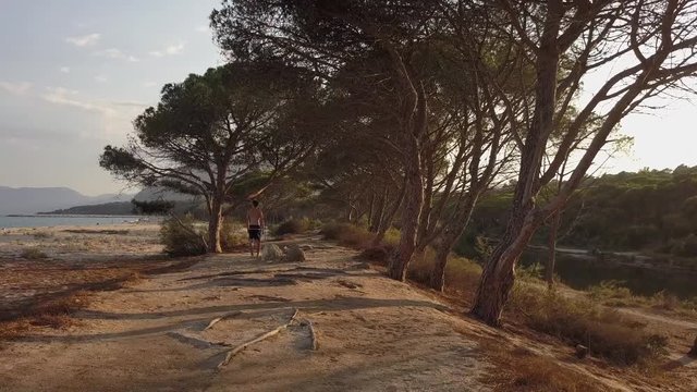 Young man walking through the trees at Cala Osalla beach, Sardinia, Italy. Mediterranean coast, with sandy beach and green vegetation. Concept of travel, tourism, holiday, exploration, trip, nature.