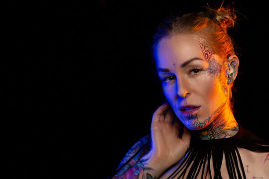 Muscled caucasian woman with tattoos and oiled skin poses under colored lights