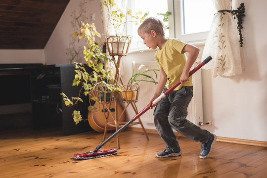 A 6-year-old boy cleaning the wooden floor with a mop