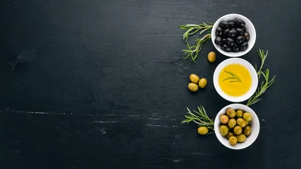Foto op Canvas Een set van olijven en olijfolie en rozemarijn. Groene olijven en zwarte olijven. Op een zwarte houten achtergrond. Vrije ruimte voor tekst. © Yaruniv-Studio