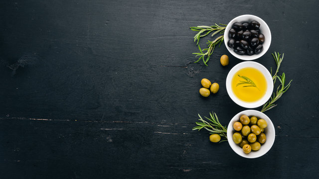 A set of olives and olive oil and rosemary. Green olives and black olives. On a black wooden background. Free space for text.