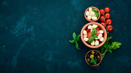 Cooking a caprese salad. Mozzarella cheese, cherry tomatoes, olives, basil leaves, oil, pepper. On...